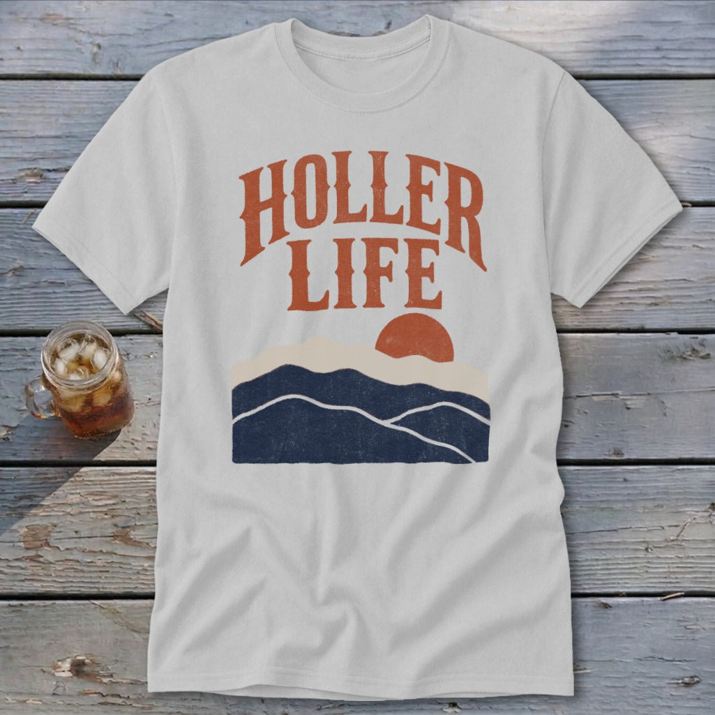 Light gray t-shirt with the text HOLLER LIFE above a sunset landscape graphic on wood background.