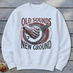 A white crewneck sweatshirt featuring a vintage graphic of a hand playing a banjo and text reading Old Sounds New Ground.