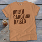 Orange t-shirt with "North Carolina Raised" text in brown block letters.