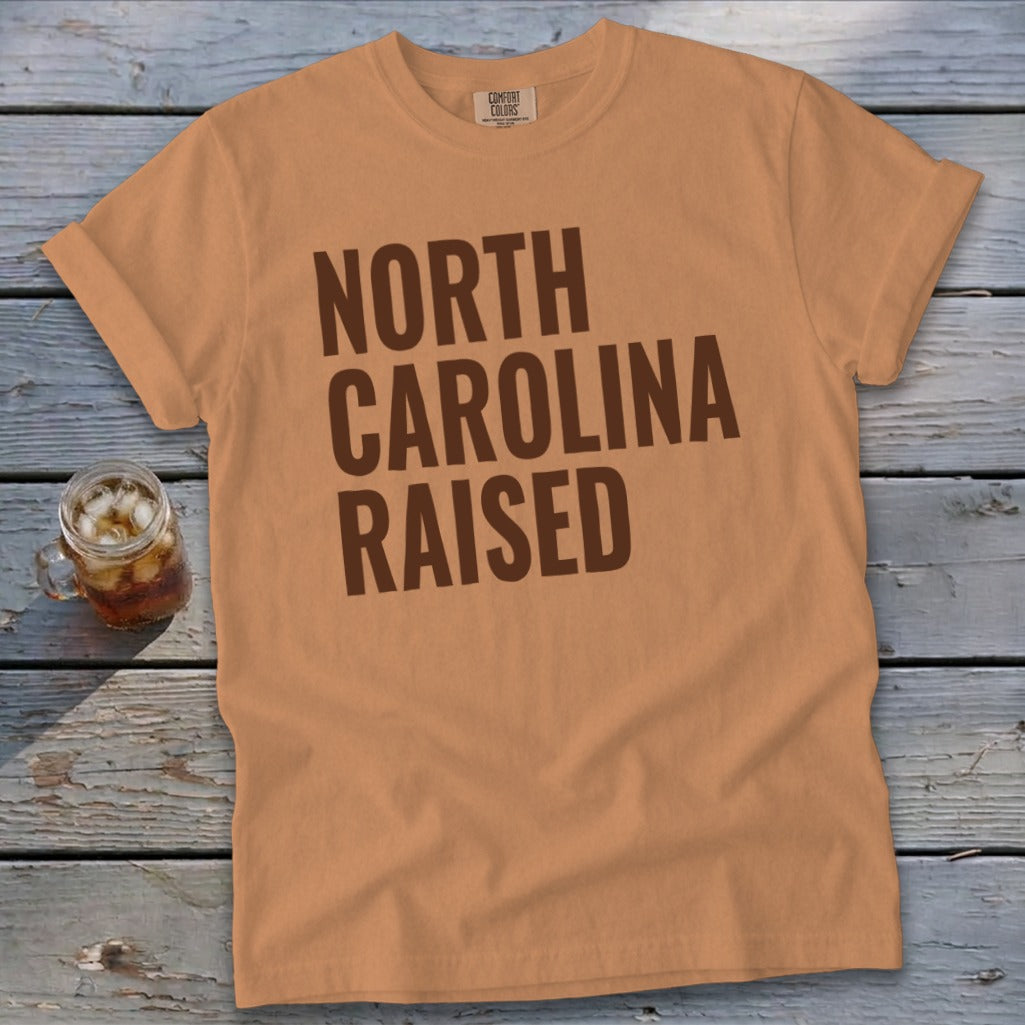 Orange t-shirt with "North Carolina Raised" text in brown block letters.