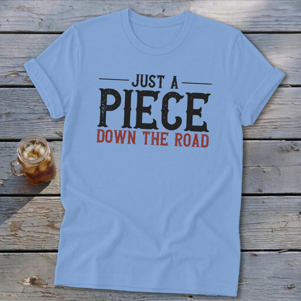 Light blue t-shirt with black and red text "JUST A PIECE DOWN THE ROAD".