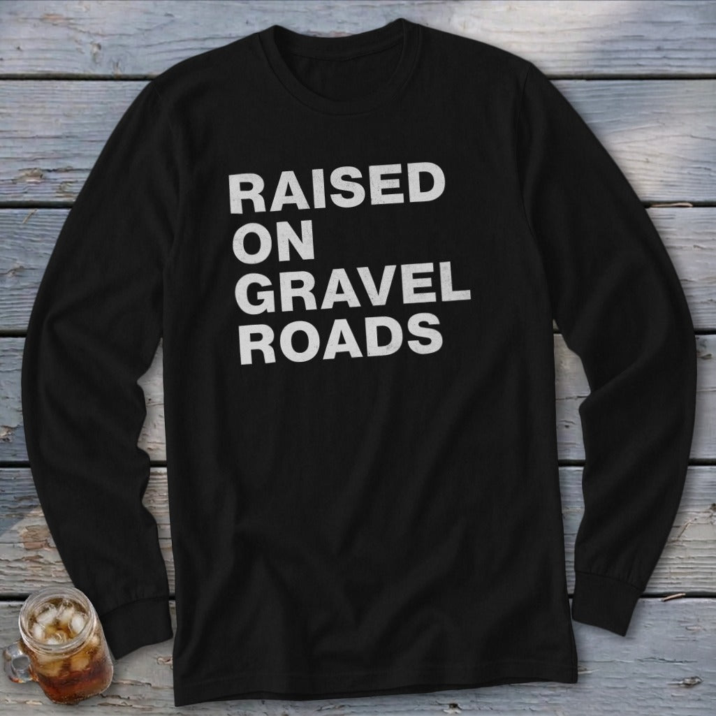Black long-sleeve shirt with white text: "RAISED ON GRAVEL ROADS"