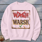 Light pink crewneck sweatshirt featuring a rustic sign graphic with the crossed-out text "WASH" and "WARSH" with a green checkmark.