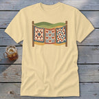 A cream-colored t-shirt with a graphic of three patchwork quilts hanging on a clothesline outdoors.