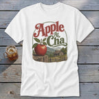 A white t-shirt featuring a retro graphic of an apple, a cabin, and the text Apple At Cha.
