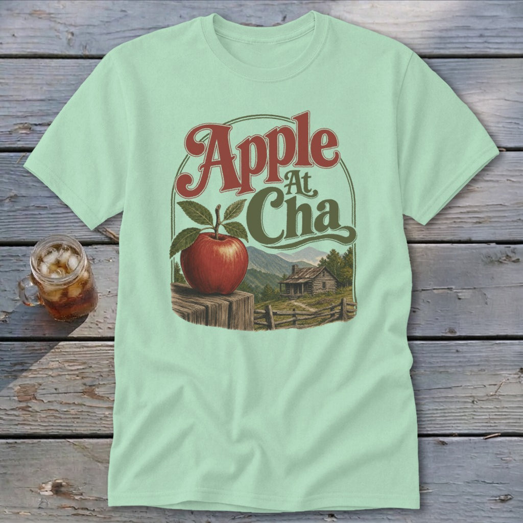 Light green t-shirt featuring a retro graphic of an apple on a fence before a mountain cabin and the text Apple At Cha.