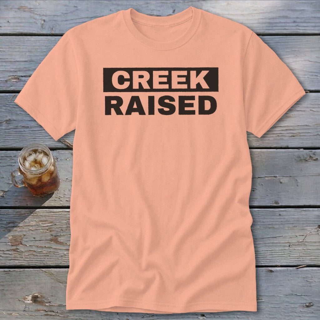 Peach t-shirt with black text "CREEK RAISED" in a rectangle.