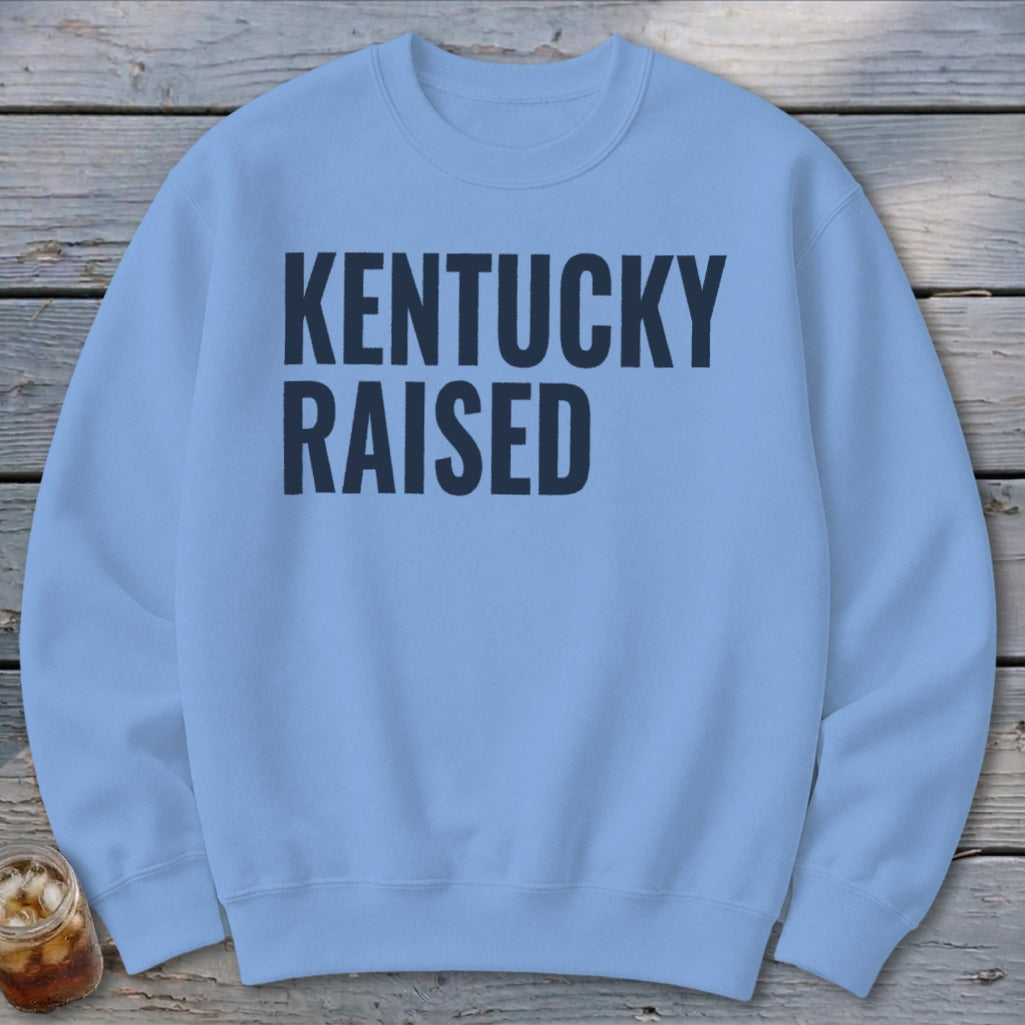 Light blue crewneck sweatshirt with "KENTUCKY RAISED" text in dark blue.