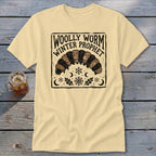 A cream-colored t-shirt with a vintage black graphic of a woolly worm caterpillar and text reading WOLLY WORM WINTER PROPHET.