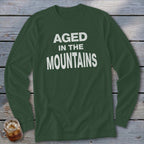 Dark green long-sleeve shirt with white text "AGED IN THE MOUNTAINS".