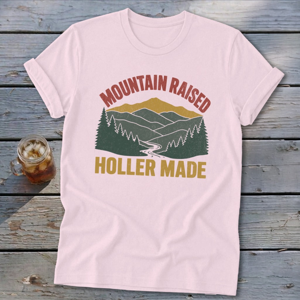 Light pink t-shirt with rolled sleeves featuring a retro mountain graphic and text reading MOUNTAIN RAISED HOLLER MADE.