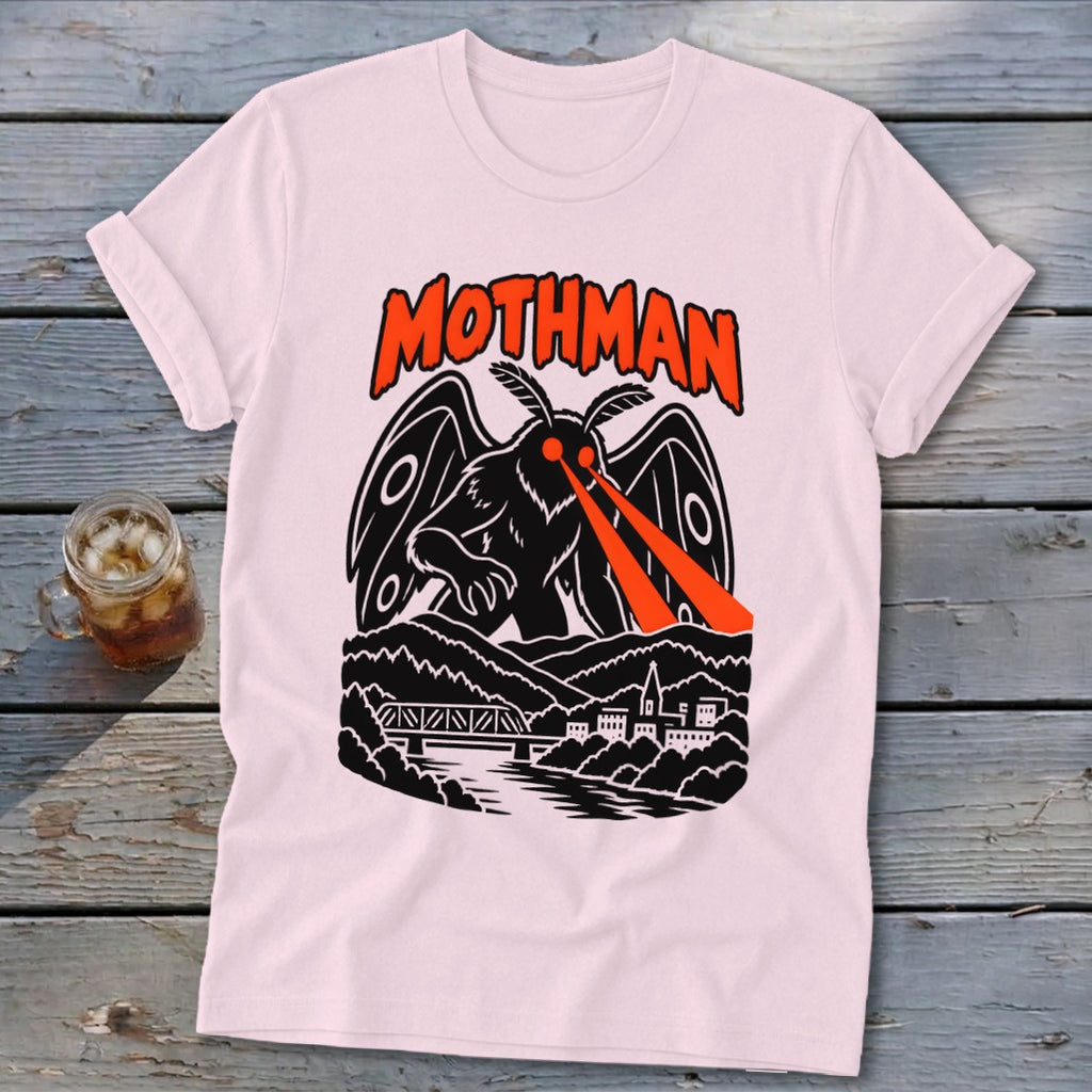 Pink t-shirt with black and orange Mothman design featuring glowing eyes and a town.