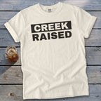 Cream t-shirt with bold black text "CREEK RAISED".