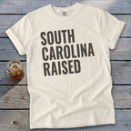 Cream t-shirt with "South Carolina Raised" printed in dark gray text.