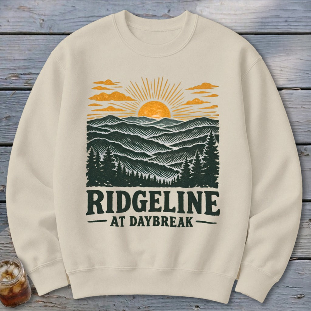 Cream sweatshirt with a graphic of mountains, sunrise, trees, and text "RIDGELINE AT DAYBREAK".