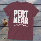Maroon crewneck t-shirt with short sleeves featuring bold white text that reads PERT NEAR above a mountain outline.
