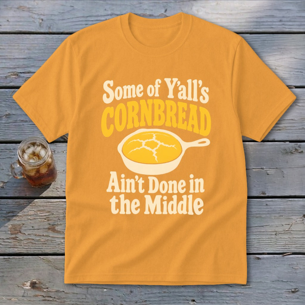 Gold t-shirt featuring a graphic of cornbread in a skillet with the text Some of Yall Cornbread Aint Done in the Middle