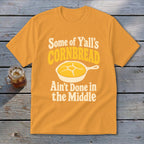 Gold t-shirt featuring a graphic of cornbread in a skillet with the text Some of Yall Cornbread Aint Done in the Middle