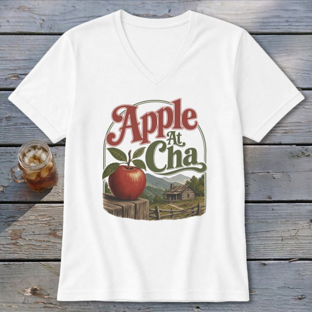 A white V-neck t-shirt featuring a retro graphic of an apple, a rustic cabin, and the text Apple At Cha.