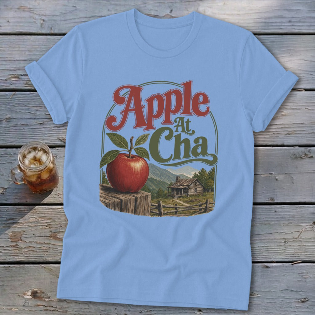 Light blue t-shirt featuring a retro graphic of an apple, a rustic cabin, and the text Apple At Cha.