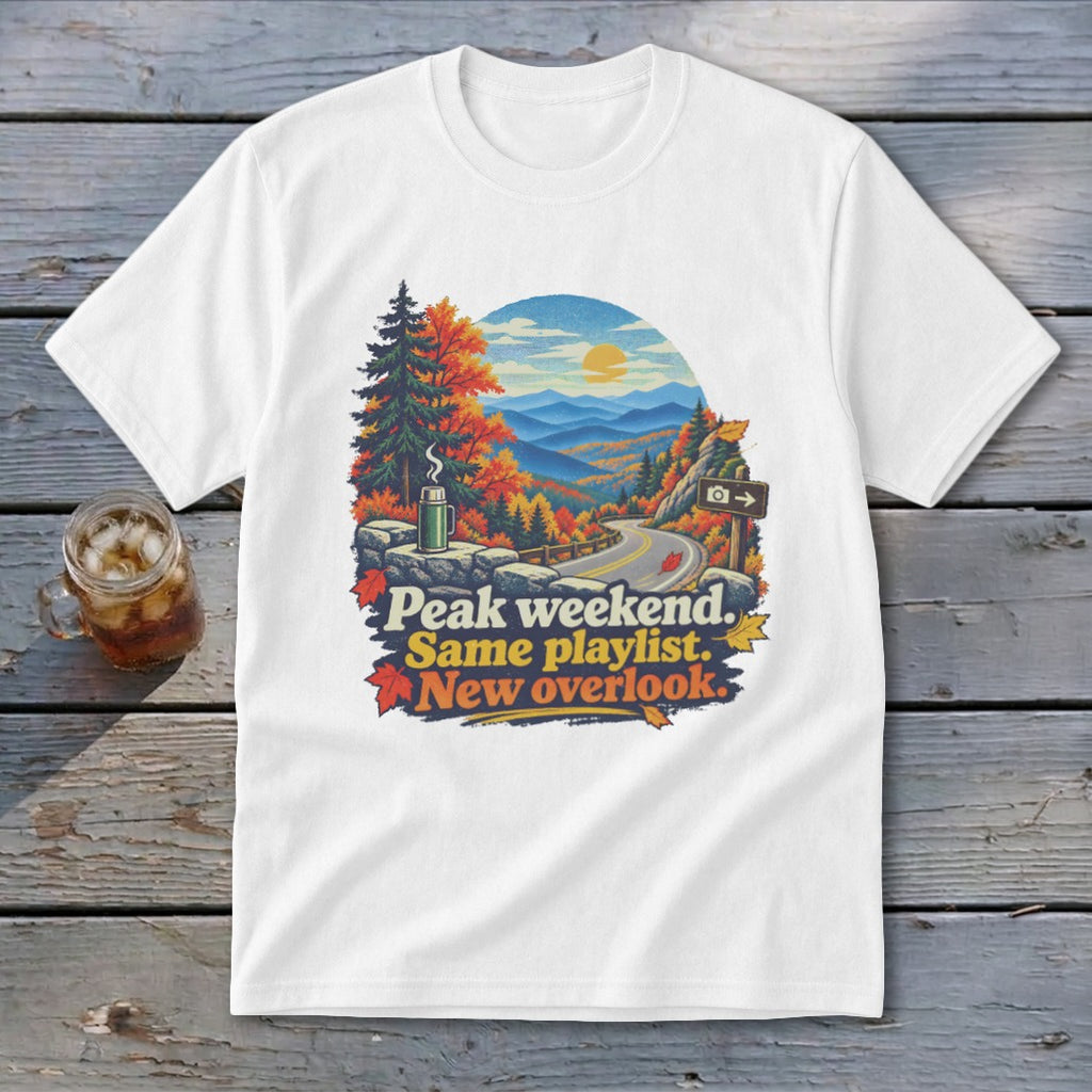 White t-shirt graphic with mountain view and text: "Peak weekend. Same playlist. New overlook."
