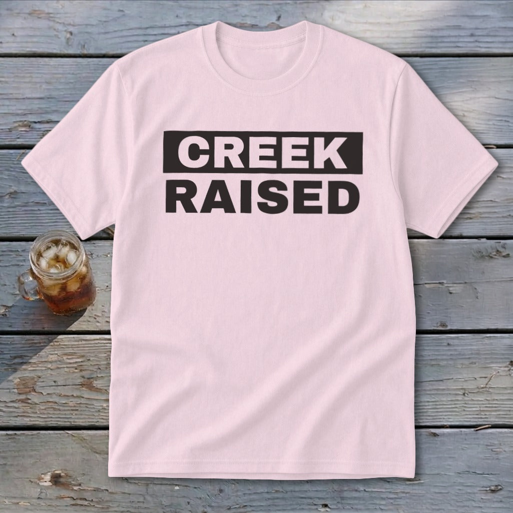 Light pink t-shirt with black text "CREEK RAISED" on a dark rectangle.