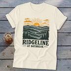 Cream t-shirt with "Ridgeline at Daybreak" text and a sunrise mountain landscape design.