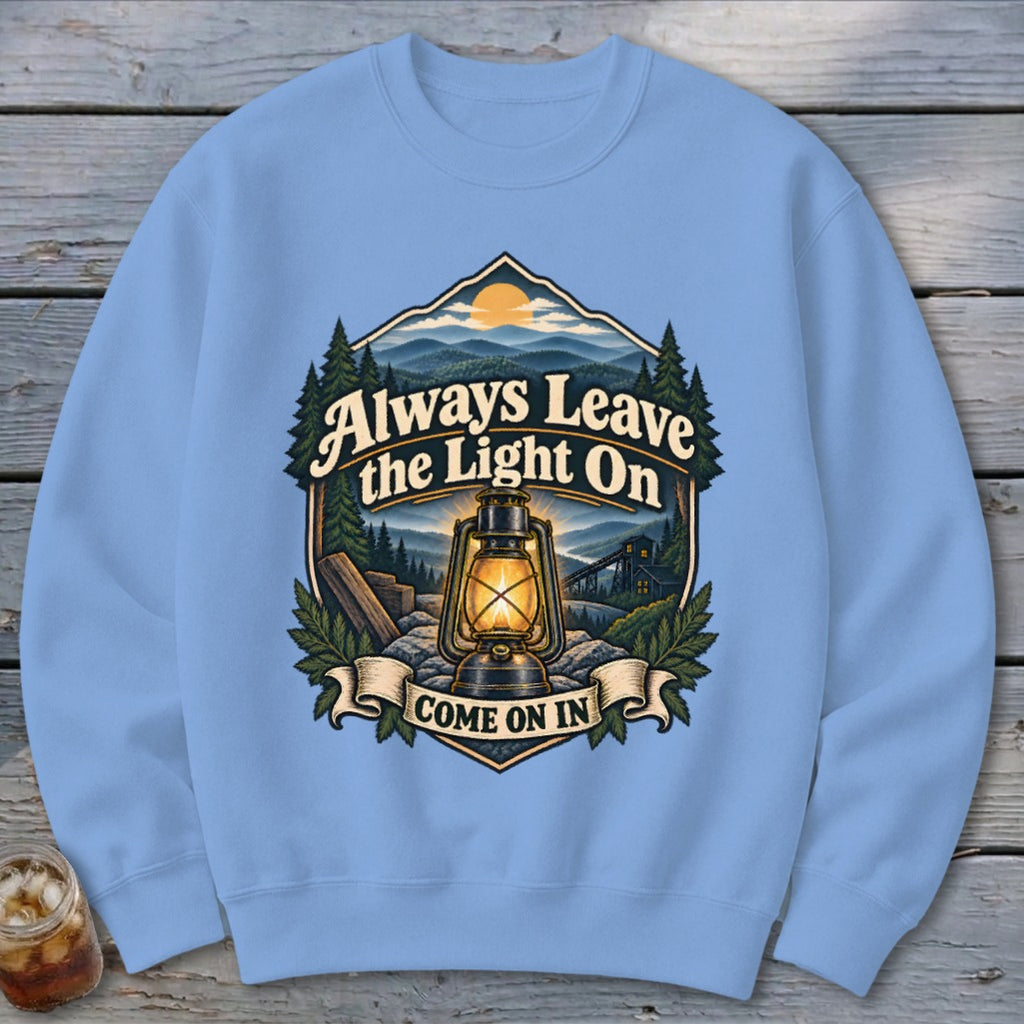 Light blue sweatshirt with a landscape design featuring a lantern and text "Always Leave the Light On COME ON IN".
