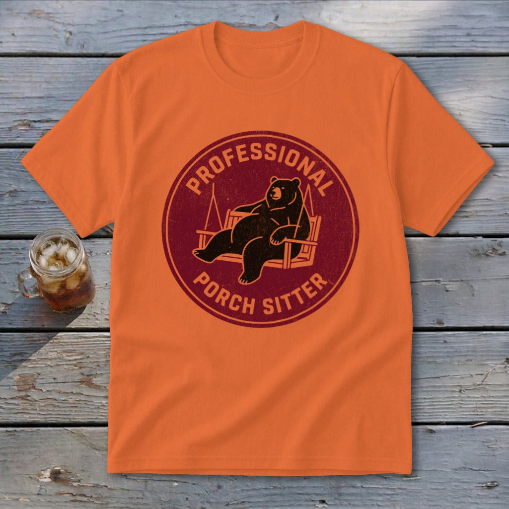 An orange t-shirt featuring a circular graphic of a bear lounging on a porch swing, with the text PROFESSIONAL PORCH SITTER.