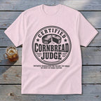 Light pink t-shirt with a black graphic reading "Certified Cornbread Judge" and an illustration of cornbread.