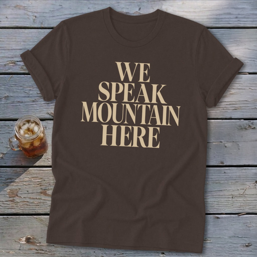 Brown t-shirt with cream text that reads "WE SPEAK MOUNTAIN HERE".
