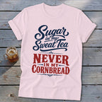 A light pink t-shirt with blue and red text reading Sugar in my sweat tea, Never in my cornbread.