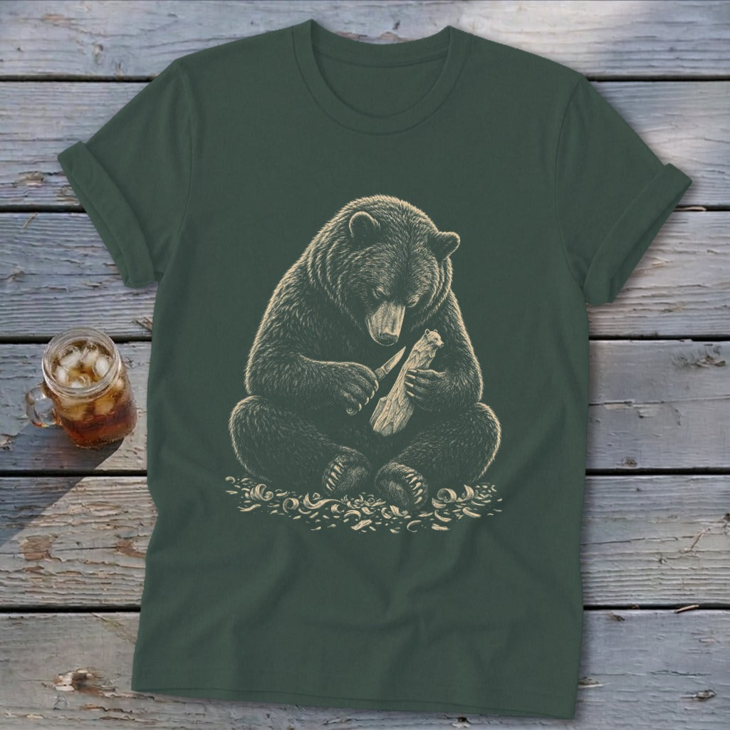 Bear carving a piece of wood with a knife on a dark green t-shirt.