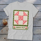 White t-shirt with a pink and cream quilt block design and "SHOO FLY" text.