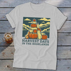 A light gray t-shirt featuring a graphic of a stack of pumpkins and hills, with the text "HARVEST DAYS IN THE HIGHLANDS".