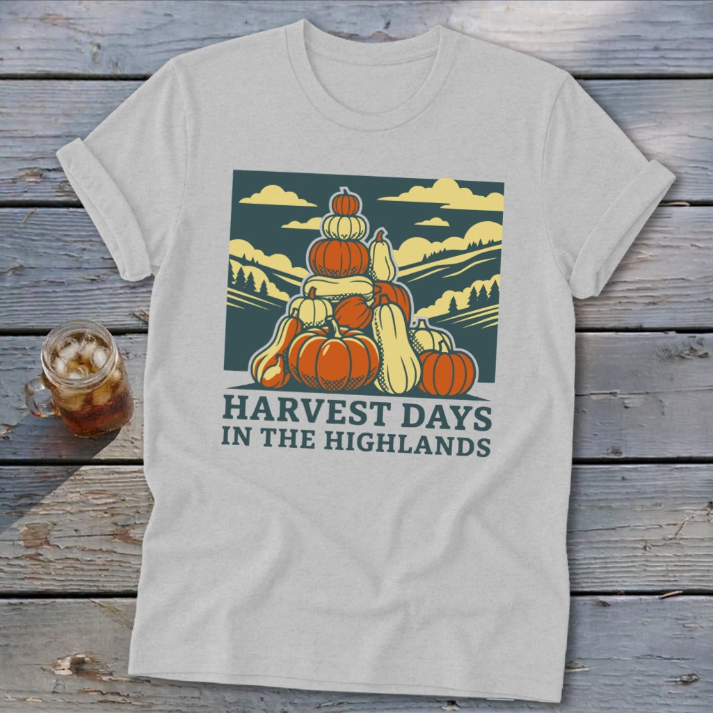 A light gray t-shirt featuring a graphic of a stack of pumpkins and hills, with the text "HARVEST DAYS IN THE HIGHLANDS".