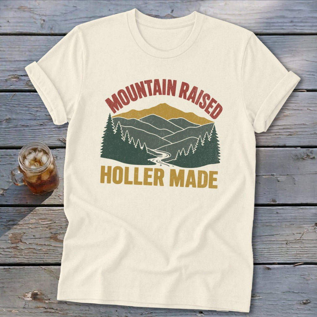 Cream-colored t-shirt featuring a retro mountain landscape graphic with the text Mountain Raised Holler Made.