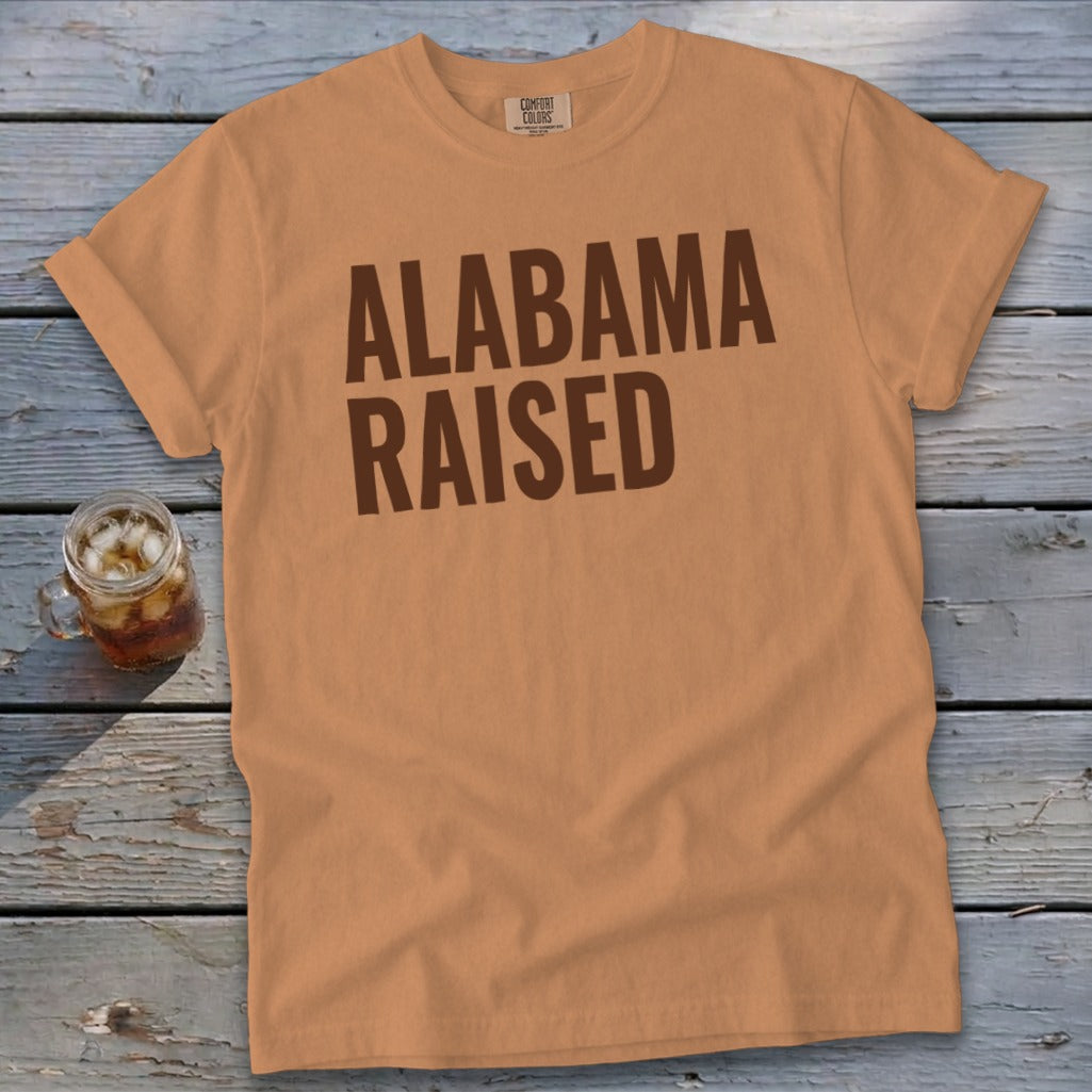 Orange t-shirt with brown text that reads "ALABAMA RAISED".