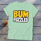 A mint green short-sleeve t-shirt with the text BUM FUZZLED on a wooden surface.