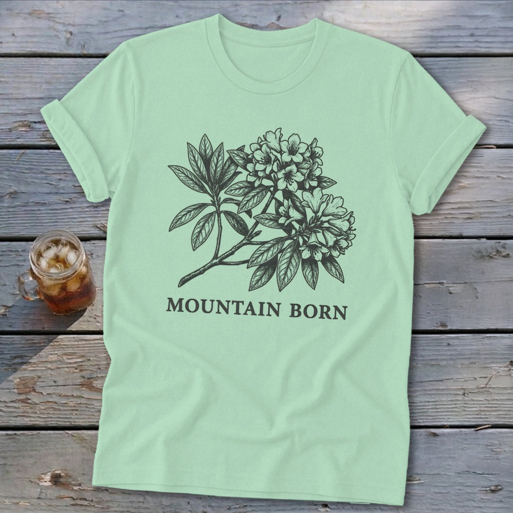 Mint green t-shirt with black line drawing of rhododendron flowers and "MOUNTAIN BORN" text.