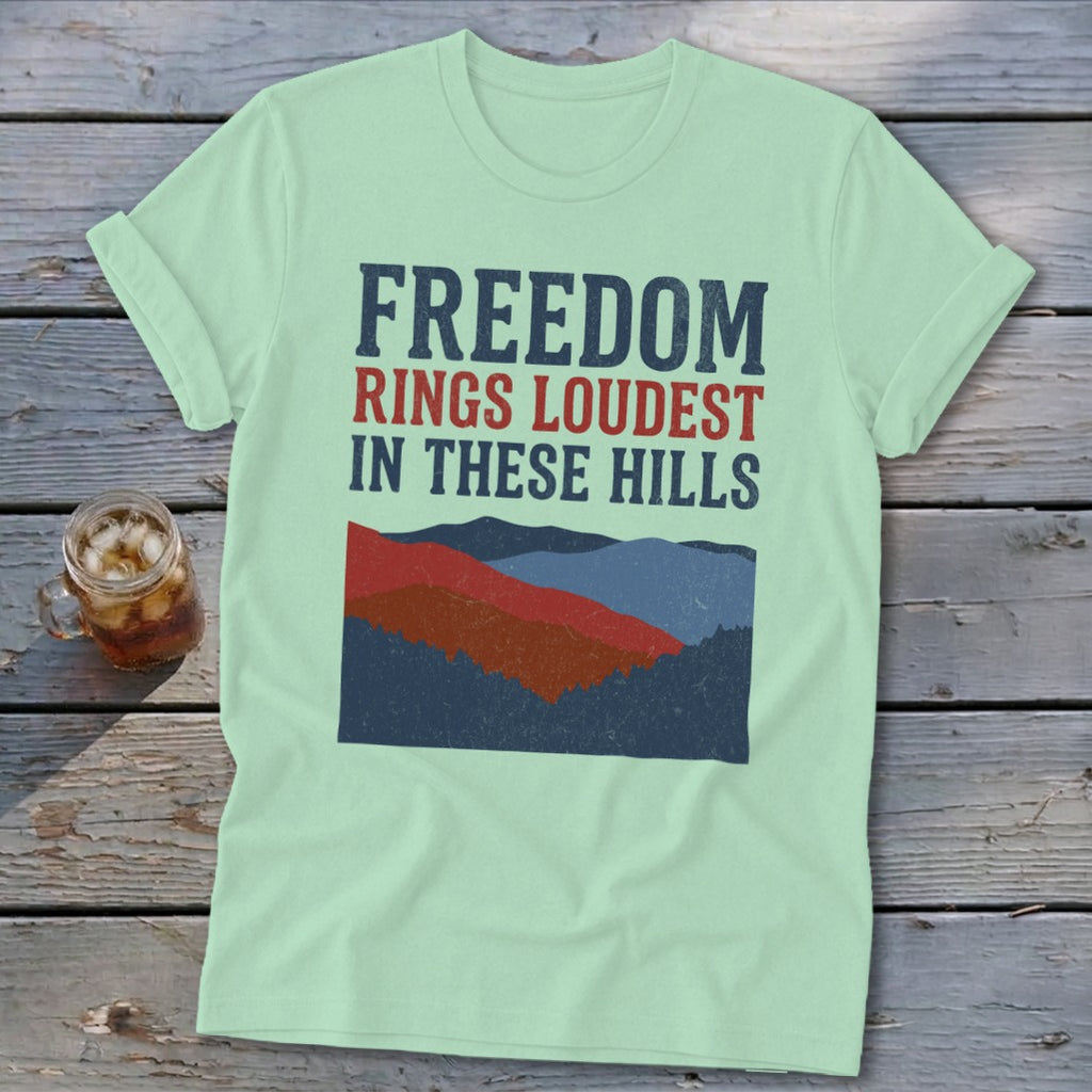 Light green t-shirt featuring the text FREEDOM RINGS LOUDEST IN THESE HILLS above a mountain illustration.