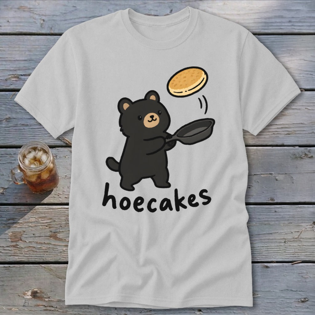 Light gray t-shirt featuring a cartoon bear flipping a pancake in a pan with the text hoecakes.