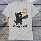 Light gray t-shirt featuring a cartoon bear flipping a pancake in a pan with the text hoecakes.