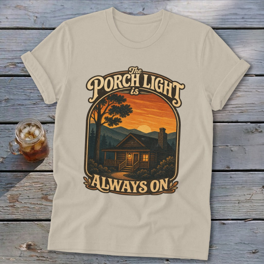 T-shirt with graphic of a cabin, sunset, and text "The Porch Light is Always On."
