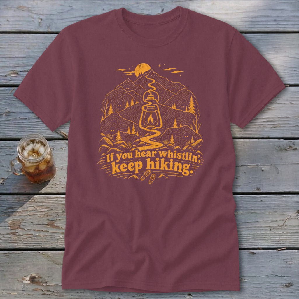Maroon t-shirt with graphic of mountains, lantern, and text "If you hear whistlin', keep hiking."