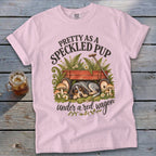 Pink t-shirt with "Pretty as a Speckled Pup Under a Red Wagon" text, dog, wagon, ferns, and mushrooms.