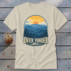 Cream t-shirt featuring a retro mountain landscape graphic with the text Over Yonder, laid on wood.