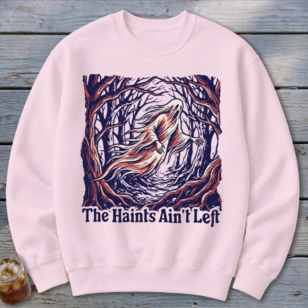 Pink sweatshirt with a ghost in a spooky forest and text "The Haints Ain't Left".