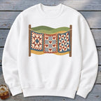 White crewneck sweatshirt with a graphic of three vintage quilts hanging on a clothesline outdoors.