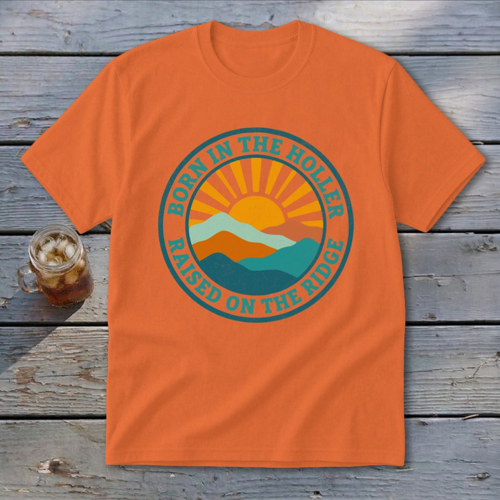 An orange crewneck t-shirt featuring a retro mountain and sun graphic with text reading Born in the Holler Raised on the Ridge.